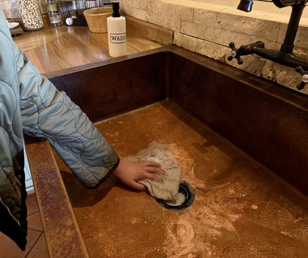 Cleaning a copper sink gently with mild soap and a soft cloth